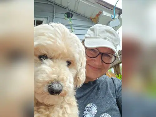 A woman with glasses and a white cap poses with a fluffy dog.